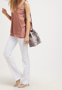 Kvinde iført en mauve ærmeløs top, hvide flared bukser, nude hæle og bærende en skuldertaske med slangeskindsprint.