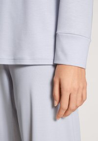 Lichtblauw langemouwen shirt met een ronde hals, zachte textuur en een manchetzoom. Hand rustend op bijpassende zachte stoffen onderkant.