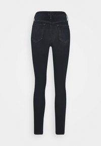 Jeans ajustados negros de tiro alto con bolsillos traseros que presentan un sutil detalle de costura, exhibidos sobre un fondo blanco liso.