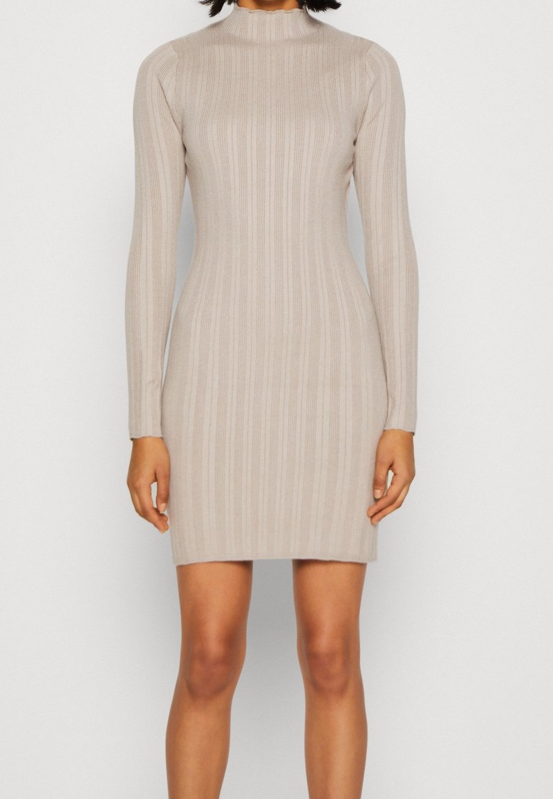 Abito lungo beige a maniche lunghe con colletto alto, silhouette aderente e taglio all'altezza dei fianchi, realizzato in un tessuto a maglia elasticizzato.