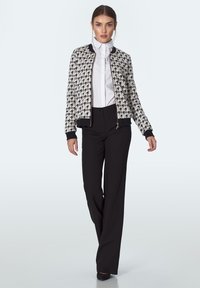 Kobieta pewnie idzie w czarno-białej kurtce w kratę, białej koszuli na guziki, czarnych szerokich spodniach i czarnych butach.