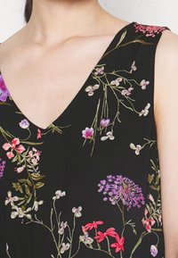 Blommig klänning i svart tyg med djup V-ringning och ärmlös design. Utsmyckad med färgglad blommig broderi i nyanser av rosa och lila.