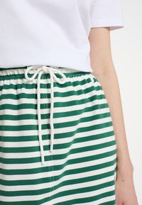 Grønne og hvide stribede shorts med elastisk talje og snor. Stoffet ser blødt ud med et afslappet design.