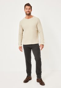Beiges Langarmshirt mit Waffelstrickmuster, lockere Passform, kombiniert mit dunkelgrauen Slim-Fit-Hosen und braunen Schnürschuhen. Schlichtes Design, weiche Textur.