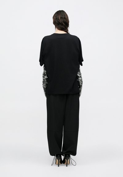 Schwarzes übergroßes T-Shirt mit kurzen Ärmeln, das strukturierte Paillettenakzente an den Seiten aufweist, und locker sitzende schwarze Hosen mit weitem Bein.