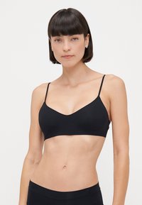 Bralette noir avec de fines bretelles réglables, design en V, texture lisse et coupe ajustée. Style simple et minimaliste.