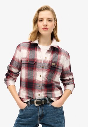 Rood, grijs en wit geblokt flanellen shirt met knoopsluitingen en twee borstzakken. Draagt over een wit shirt en gecombineerd met blauwe denim jeans.