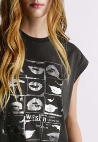Camiseta gráfica negra con mangas cortas extragrandes, con estampados de labios plateados en diseño de cuadrícula y texto "WEST 11 NOTTING HILL" y fecha.