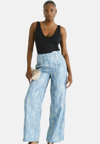 Blue high-waisted wide-leg jeans with a textured finish, featuring a large belt and a small silver handbag. Model in a black tank top.