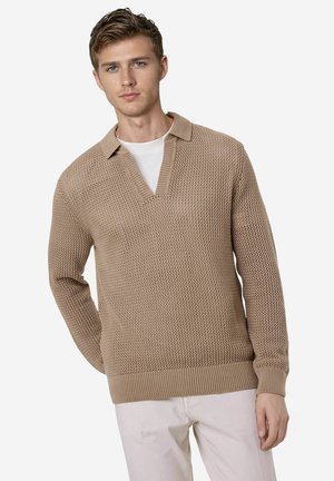 Beige gestrickter Pullover mit Polo-Kragen, ausgestattet mit einem strukturierten Muster sowie gerippten Bündchen und Saum, getragen über einem weißen T-Shirt.