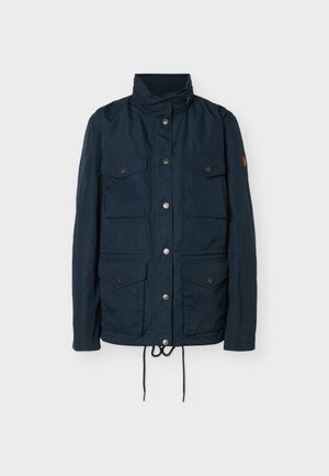 Jachetă bleumarin cu guler înalt, fermoar frontal acoperit cu nasturi capse, patru buzunare cu clape și capse, și șnururi ajustabile la tiv.