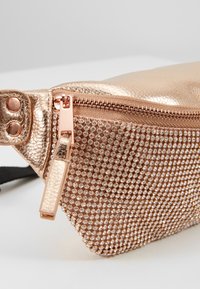 Pochette in oro rosa metallico con superficie texture, decorazioni in strass e chiusura con zip dotata di un piccolo tirante.