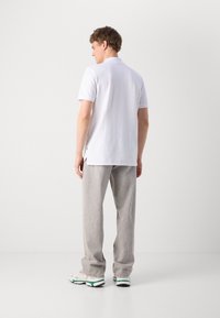 White short-sleeved polo shirt with a collar, back slit detail, paired with light gray textured trousers and sporty shoes with green accents.