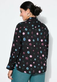 Svart skjorta med ett mönster av flerfärgade juvelformer i rosa, blå och grön. Långa ärmar och knäppt krage. Slät textur.