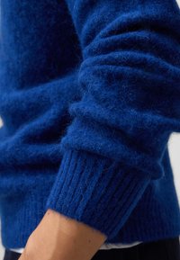 Królewskie niebieski sweter o miękkim, teksturowanym, puszystym splocie. Posiada prążkowane mankiety i dół. Zbliżenie podkreśla szczegóły materiału.