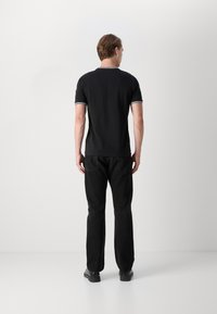 Sort polo skjorte med korte ærmer og hvidt trim på kraven og ærmerne, parret med lige ben sorte jeans og sorte sko.