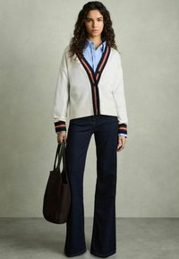 Vit kortärmad cardigan med marinblå och orange ränder, knappad fram; ljusblå skjorta under. Mörka utsvängda jeans; svart axelväska.