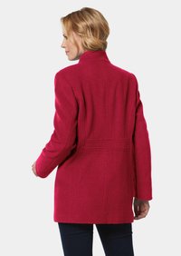 Fuchsia-Mantel aus Wolle-Mix, mit gerader Silhouette, hohem Kragen und Nahtdetails auf der Rückseite. Lange Ärmel und minimale Hardware.