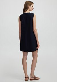 Vestido sin mangas azul marino con corte recto, que presenta una costura trasera sutil y un cierre de cremallera en el cuello. Se lleva con sandalias marrones.
