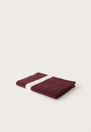 Serviette rouge foncé pliée avec une large bande blanche unique, posée sur un fond clair uni.