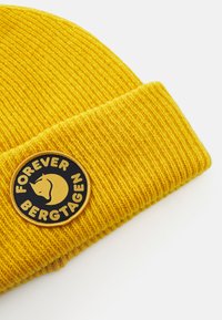 Căciulă tricotată cu model rib și galben, având o insignă rotundă neagră și galbenă cu un cap de rinocer și textul "Forever Bergtagen".