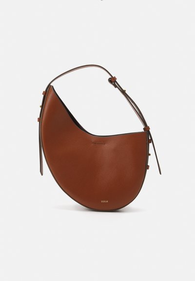 Sac à épaule en cuir marron avec une forme en croissant, une fine bandoulière marron et des accents subtils en métal doré. Présente une texture lisse et des coutures minimales.