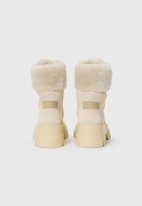 Beige winterlaarzen met een pluizige rand en een dikke zool, met een logo-label aan de achterkant, weergegeven tegen een effen witte achtergrond.