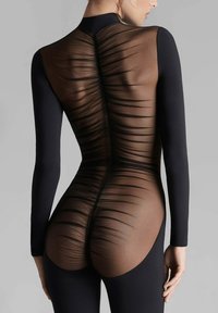Bodysuit noir à manches longues, avec un dos transparent et côtelé qui contraste avec le matériau lisse. Remarquable pour son texture et son design complexes.