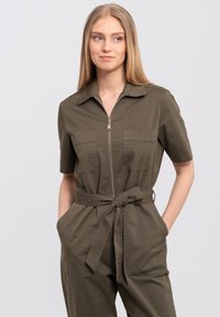 Olive green jumpsuit with short sleeves, zip front, two chest pockets, and a tie belt. Made from a lightweight, textured fabric.