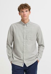 Lys grå skjorte med knapper laget av mykt materiale, med brystlomme, lange ermer og krage; inkluderer hvite knapper.