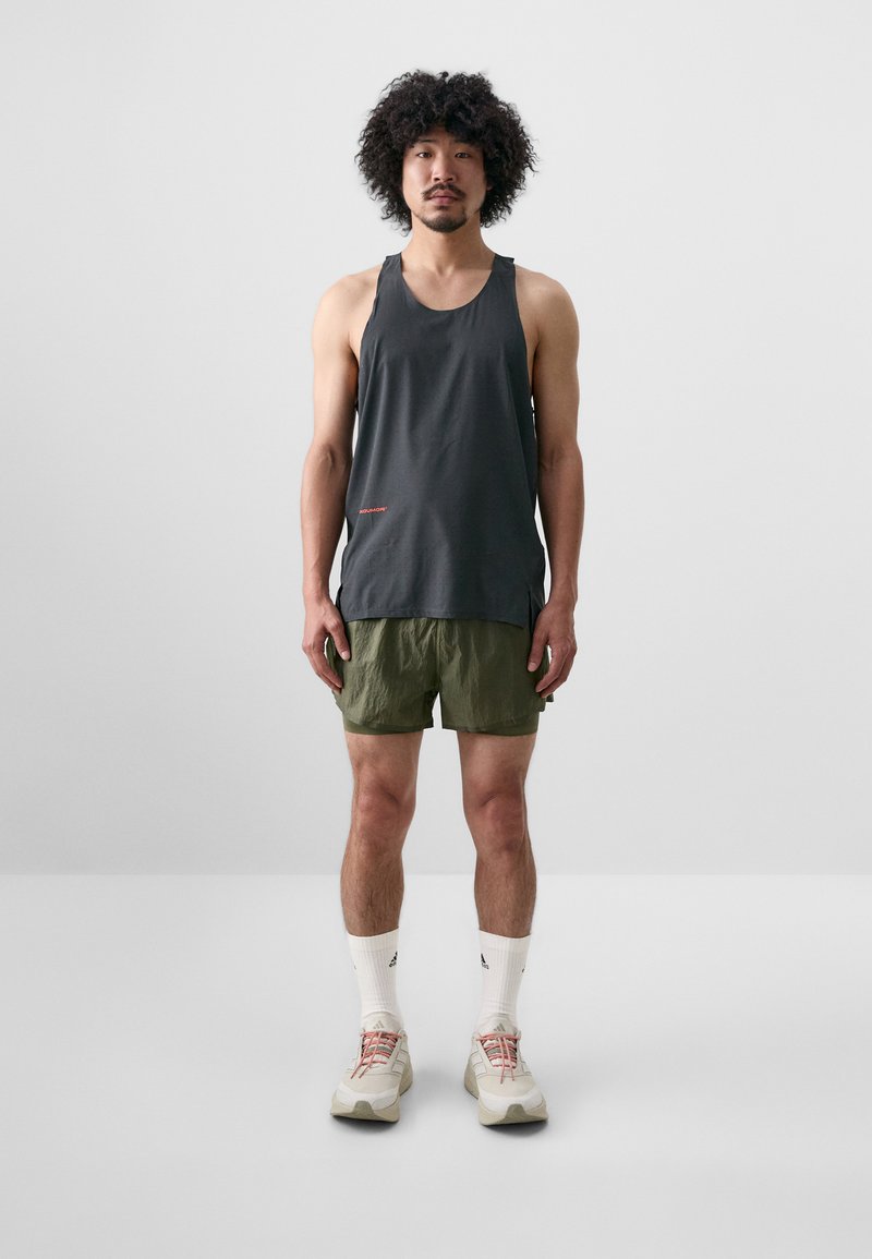 Gray sleeveless tank top with a subtle red logo, paired with lightweight olive green shorts, white adidas socks, and beige athletic shoes.