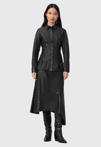 Sort læder skjorte med en tætsiddende silhuet og knaplukning, parret med en flydende sort læder nederdel og knæhøje læder støvler.