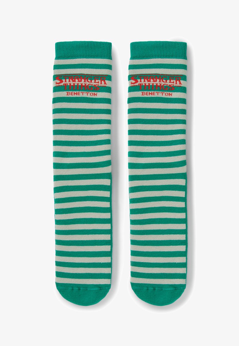 Chaussettes rayées vertes et beiges avec le texte « Stranger Things Benetton » en rouge près du haut sur un fond blanc.