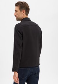 Zwarte lichte jas met een kraag, gestructureerde schouders en met knopen afgesloten manchetten, gecombineerd met donker denim. Gladde stof en minimalistisch ontwerp.