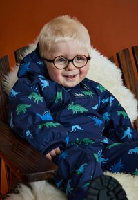 Navy vanntett snowsuit med dinosaurmønstre i grønn og blå. Har glidelås, elastiske mansjetter og et koselig indre fôr.