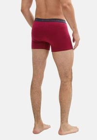 Bóxer burdeos con tela elástica, con una cinturilla en azul marino impresa con "TOM TAILOR" en rojo. Textura suave, diseño ajustado.