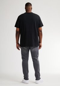 Camiseta de algodón negra con mangas cortas, corte relajado, combinada con jeans de mezclilla gris, que presentan un corte recto y un sutil desgaste.