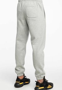 Pantalones de chándal grises fabricados en una tela suave, con cinturilla elástica, puños ajustados y un bolsillo trasero. Combinados con zapatillas deportivas negras con acentos amarillos.