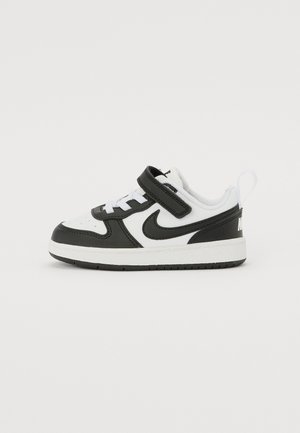 Baskets pour tout-petits en noir et blanc avec bride Velcro, logo Nike swoosh et semelle texturée sur un fond blanc uni.
