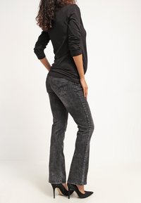 Top nero a maniche lunghe abbinato a jeans grigi a zampa d'elefante. Tessuto in denim; i jeans presentano un design con tasche posteriori. Indossato con scarpe con tacco nere.