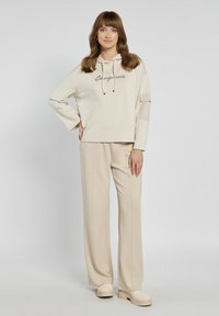 Beżowa bluza z kapturem i haftem z przodu, w połączeniu z pasującymi spodniami z szerokimi nogawkami. Miękka tkanina o gładkiej fakturze, minimalistyczny design.