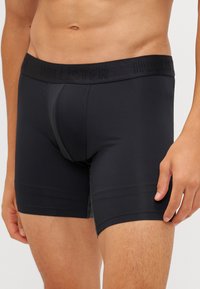 Fekete boxer alsónadrág, rugalmas anyagból készült, puha derékrésszel, amelyen a "Hollister" logó dombornyomott, és testhezálló kialakítással rendelkezik.