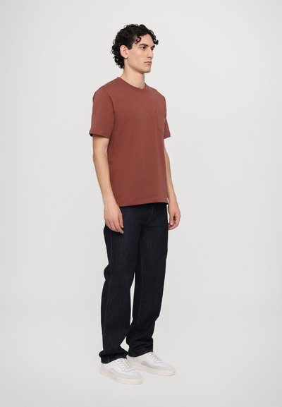 T-shirt en coton rouille à manches courtes avec poche sur la poitrine, associé à un jean en denim noir et des baskets blanches. Design simple sans motifs.