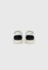 Sneaker bianchi e neri con tomaia in pelle liscia, forma arrotondata e suola testurizzata. Include dettaglio del logo sul tallone.