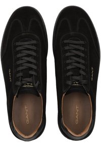 Black suede sneakers with a round toe, dark lace-up fastening, and brown leather insole. Gold logo detailing on the side. Lightweight design.