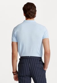 Světle modrá polo košile s krátkým rukávem a žebrovaným límcem, spárovaná s námořnickými kalhotami s jemným proužkem, které mají kapsy a malé kovové detaily.