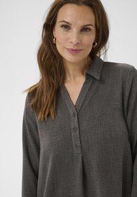 Camicia grigia con colletto, tessuto texturizzato e maniche lunghe. Presenta una chiusura con bottoni sul davanti e una vestibilità comoda.