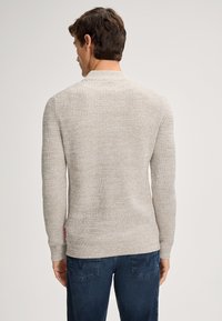 Jasno beżowy sweter z dzianiny o teksturowanym wzorze, okrągłym dekolcie i długich rękawach. Posiada metkę po lewej stronie blisko dolnej krawędzi.