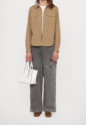 Chemise beige à manches longues avec deux poches poitrine, pantalon cargo gris, chaussures marron et sac à main blanc avec des accents noirs. Coupe structurée et décontractée.