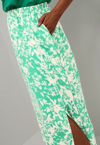 Sukňa s kvetinovým vzorom v zelenej a bielej farbe, vyrobená z mäkkej látky. Má elastický pás a bočné vrecká, s rozparkom až po stehno.